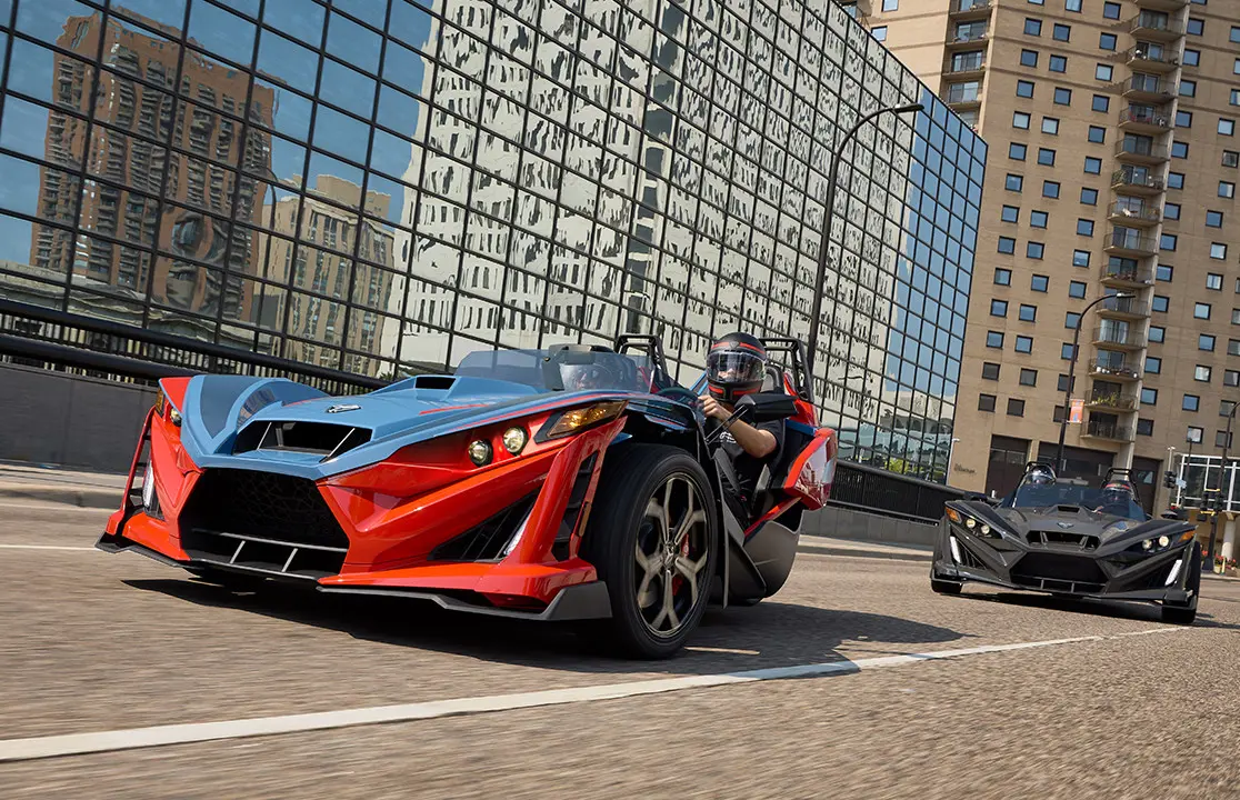 Two 2025 Polaris Slingshot R three-wheeled roadsters cruising down a city street.