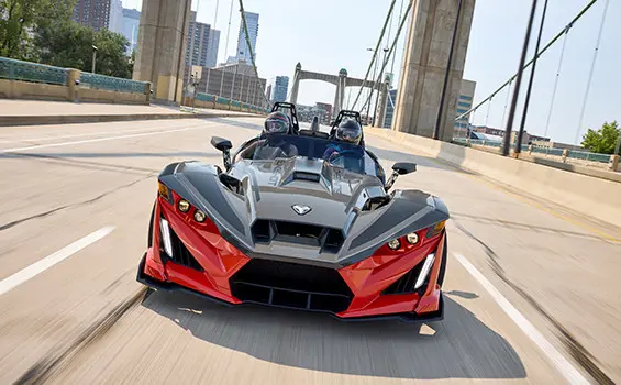 Front-end focused view of a 2025 Polaris Slingshot R three-wheeled roadster cruising down a city street.