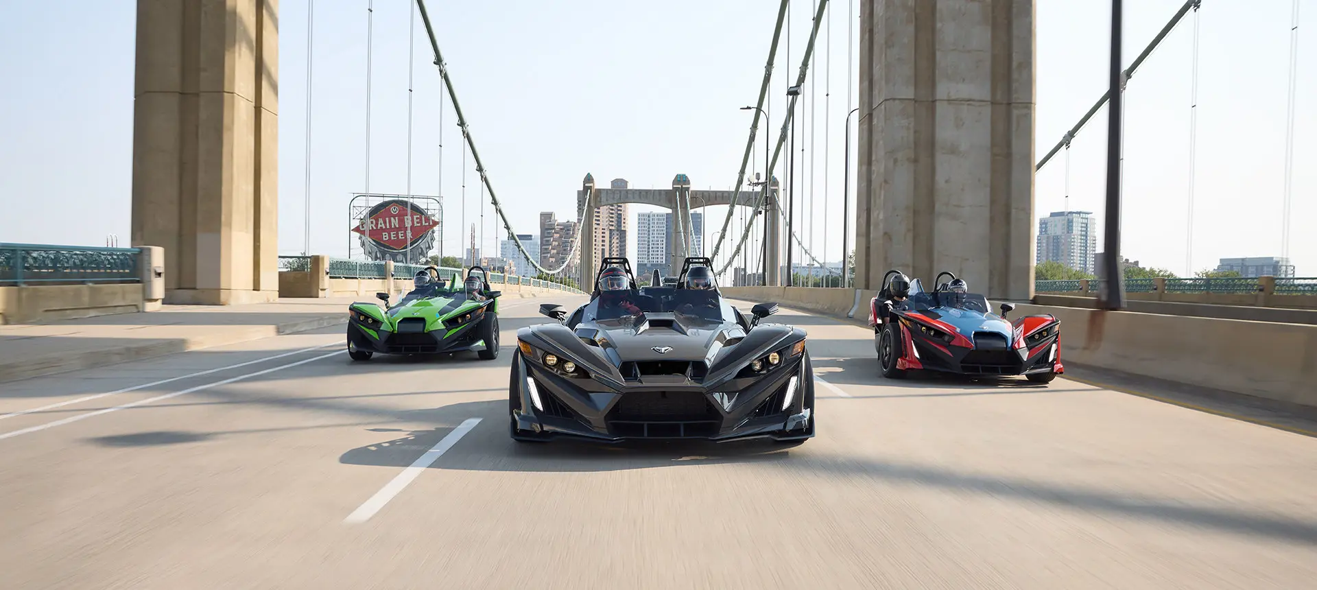 3 2025 Polaris Slingshot R three-wheeled motorcycles cruising down a city street.