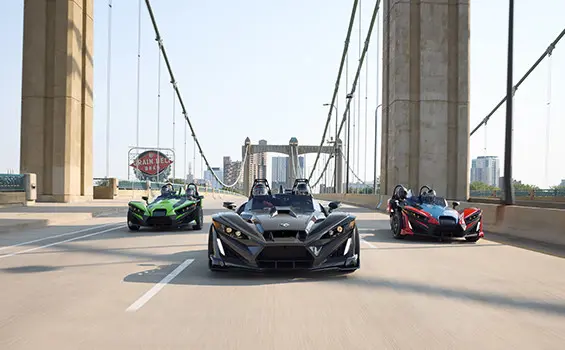 3 2025 Polaris Slingshot R three-wheeled motorcycles cruising down a city street.