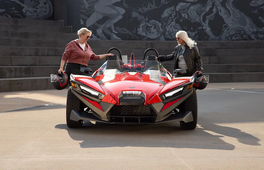 2 women with helmets stepping into a 2026 Polaris Slingshot S.