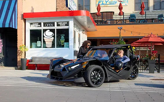 A woman speaking to a man in the driver's seat in a 2026 Polaris Slingshot S.