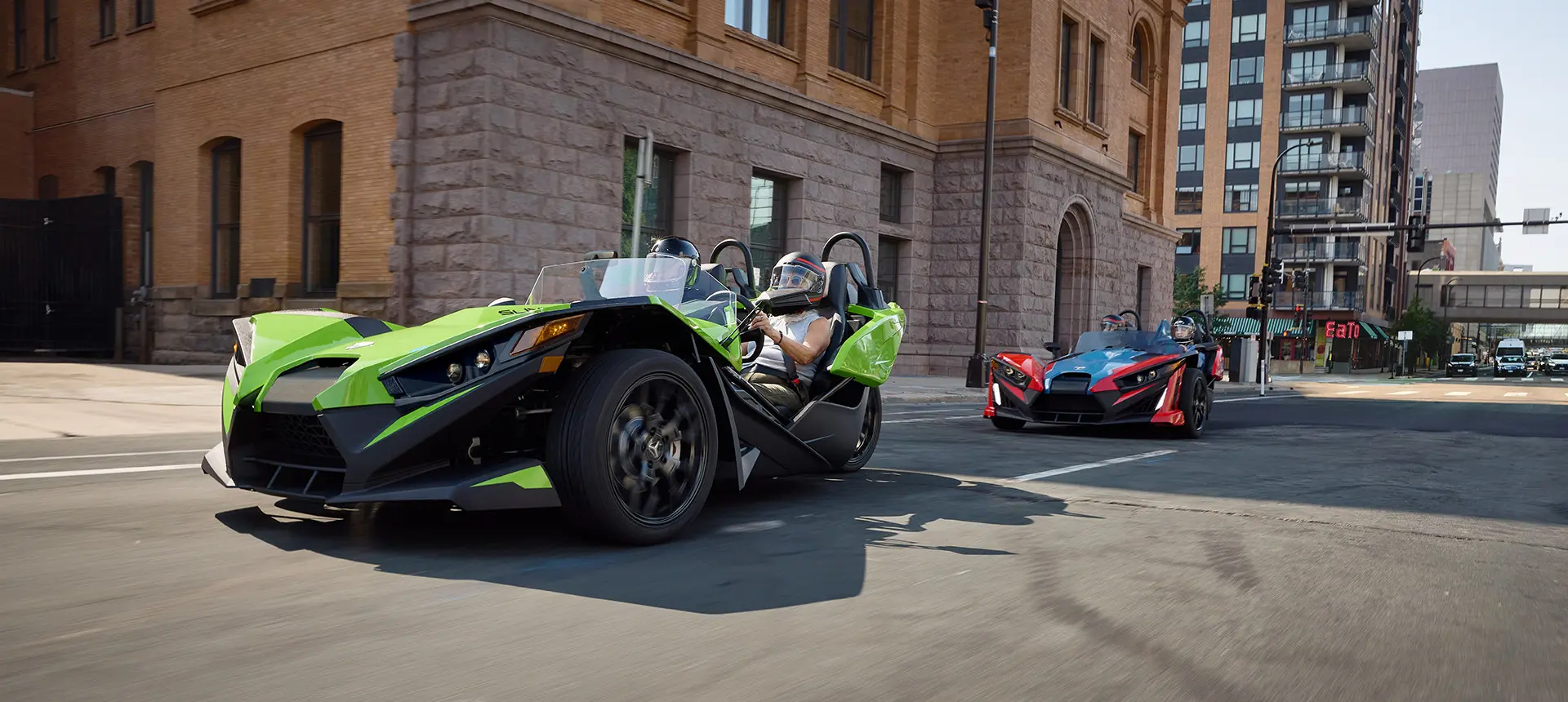 Two 2025 Polaris Slingshots cruising down a city street.