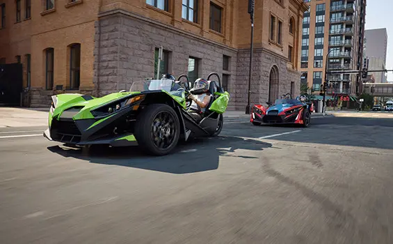 Two 2025 Polaris Slingshots cruising down a city street.