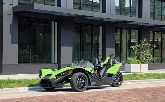 Side profile of a Liquid Lime 2025 Polaris Slingshot SL roadster parked outside a modern building.
