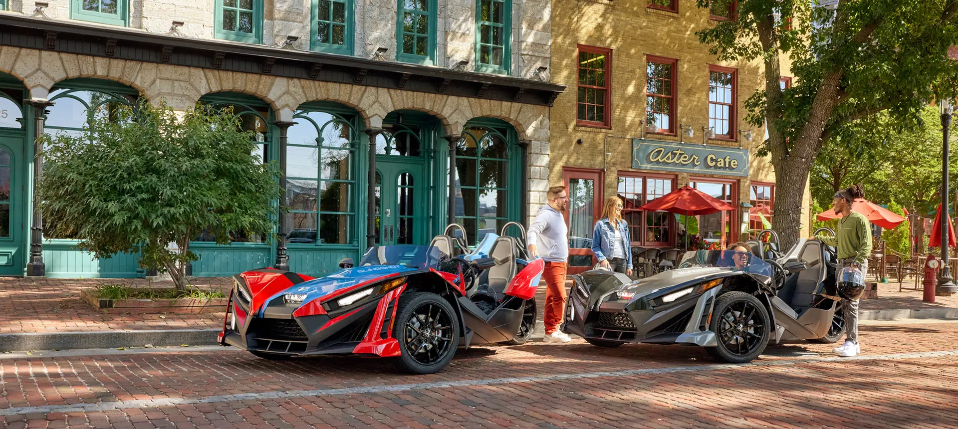 4 people chatting after a ride in their 2 Polaris Slingshot SLR roadsters.