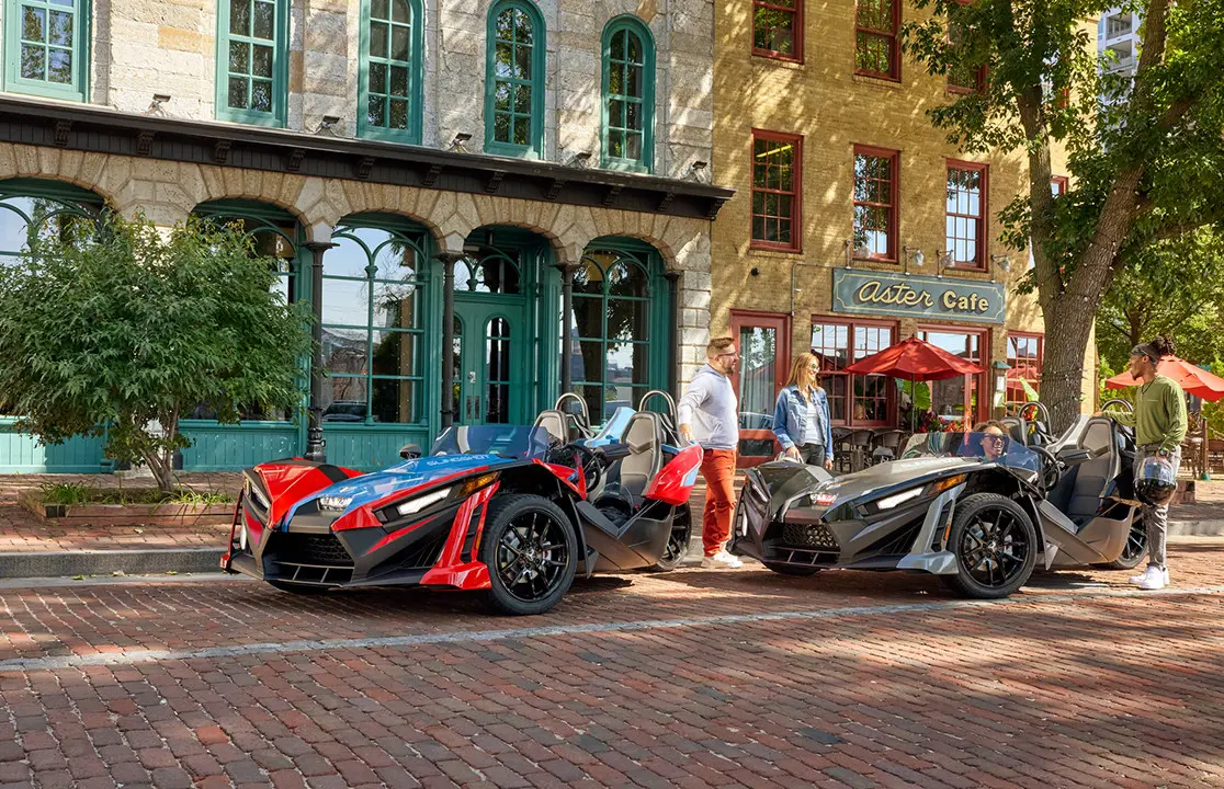 4 people chatting after a ride in their 2 Polaris Slingshot SLR roadsters.