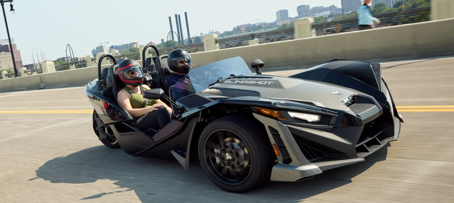 Two 2025 Polaris Slingshot SLR three-wheeled motorcycles parked in front of a steel-sided building.