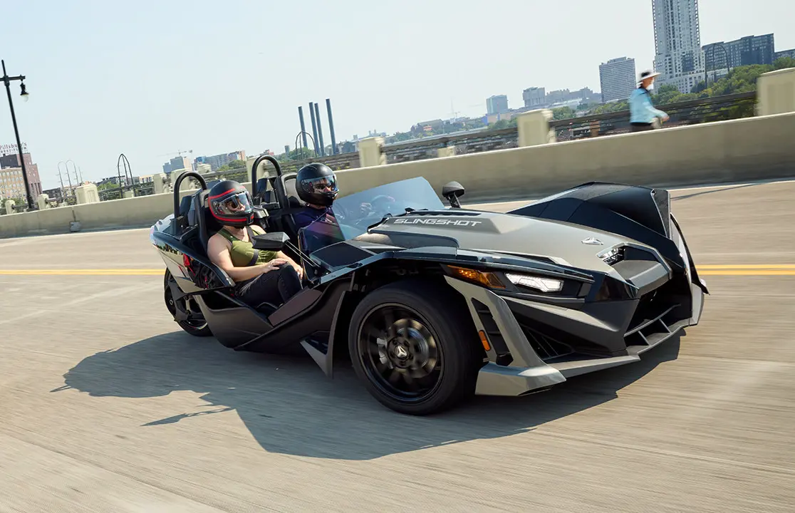 Dos motocicletas de tres ruedas Polaris Slingshot SLR de 2025 estacionadas frente a un edificio que tiene los lados de acero.