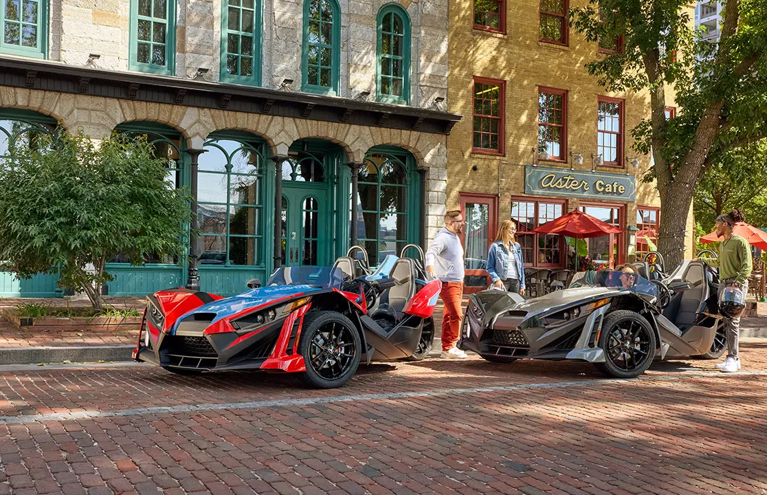 4 people chatting after a ride in their 2 Polaris Slingshot SLR roadsters.