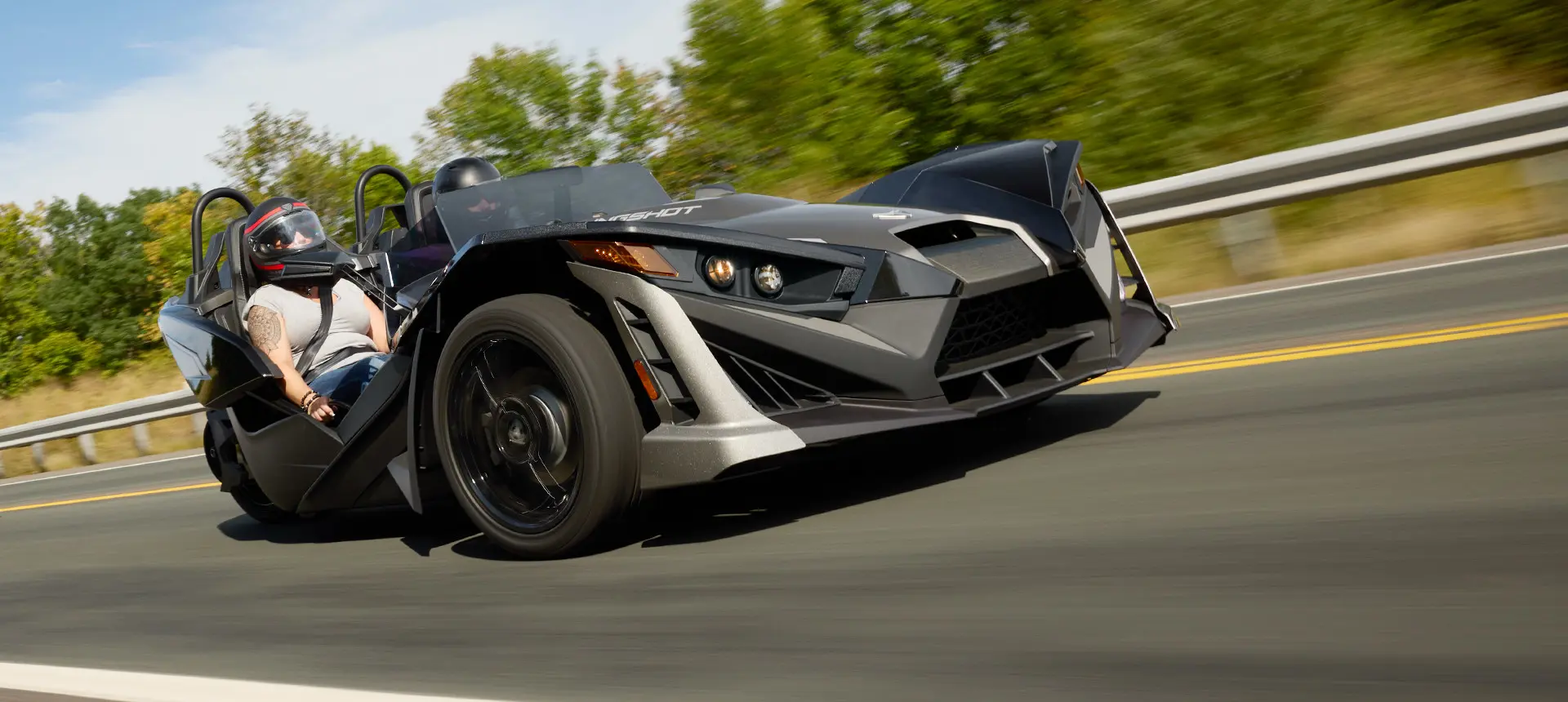Two 2025 Polaris Slingshot SLR three-wheeled motorcycles parked in front of a steel-sided building.