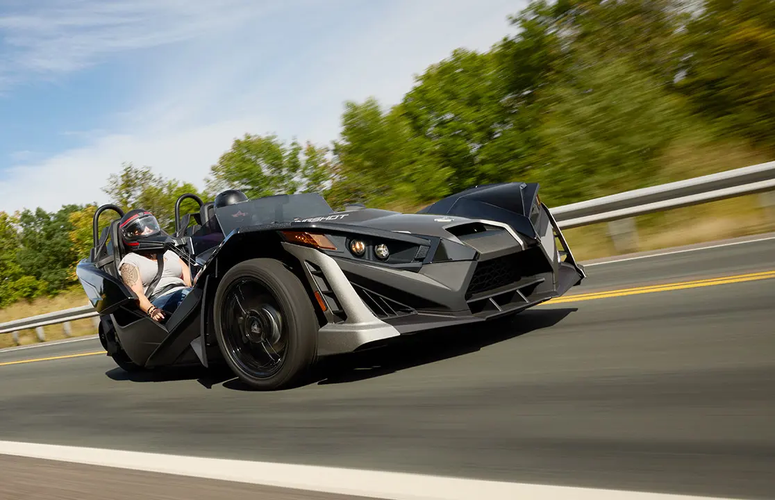 Two 2025 Polaris Slingshot SLR three-wheeled motorcycles parked in front of a steel-sided building.