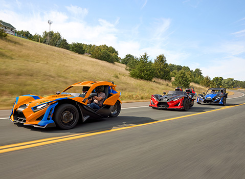 3 Polaris Slingshot vehicles cruising on the road with upgraded parts and accessories. 