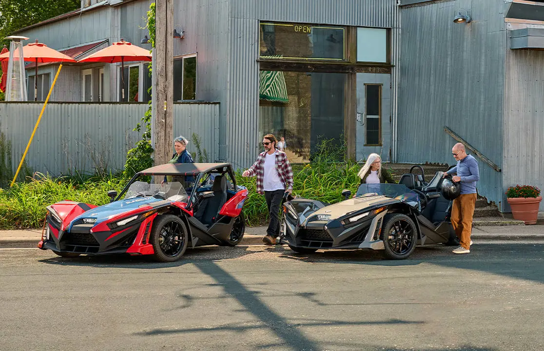 Pasajeros saliendo de vehículos Slingshot estacionados, ambos equipados con mejoras de accesorios.