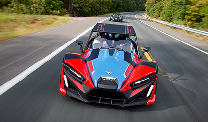 Two Polaris Slingshot vehicles in a parking lot in front of a building
