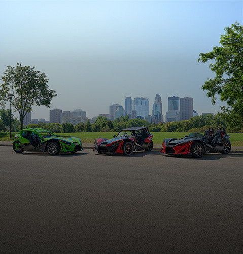 Three Polaris Slingshot vehicles parked with downtown skyscrapers in the distance.