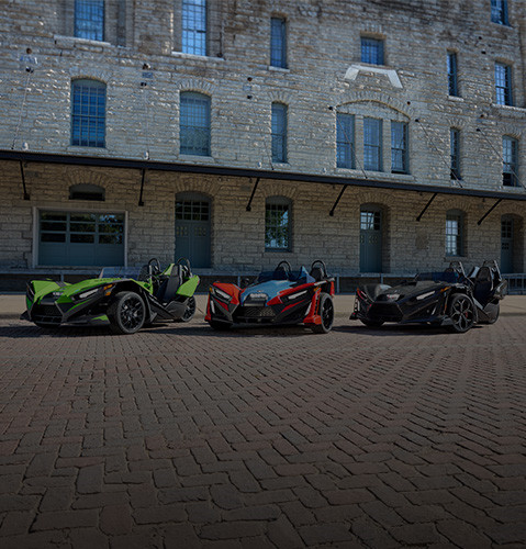 Three parked Polaris Slingshot vehicles in front of brick building.