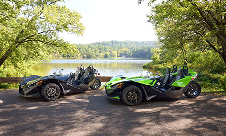 Two Polaris Slingshot SL roadsters parked near a lake.