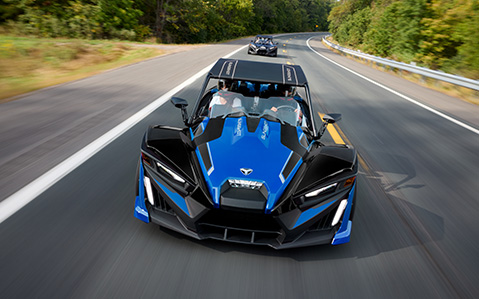 2 people in a Polaris Slingshot with custom accessories installed cruising down the highway.