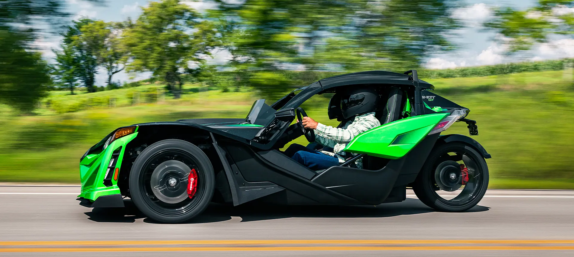 Side profile of a 2026 Polaris Slingshot Grand Touring limited edition three-wheeled roadster cruising down the road.