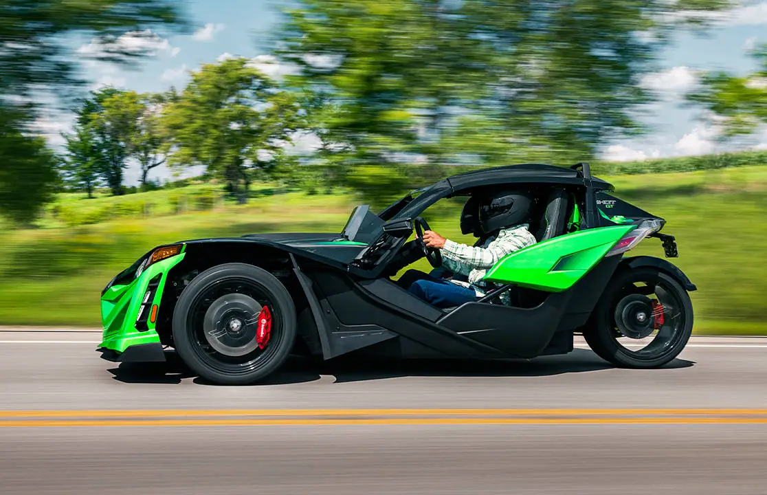 Side profile of a 2026 Polaris Slingshot Grand Touring limited edition three-wheeled roadster cruising down the road.