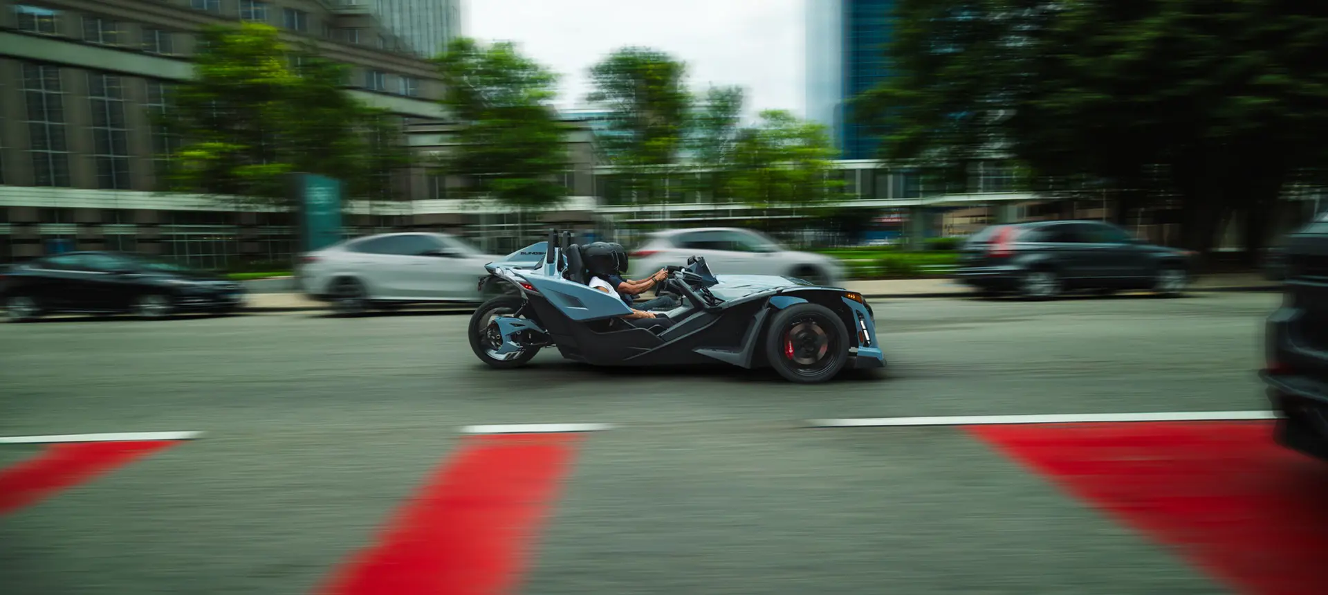 Side profile of a 2026 Polaris Slingshot Signature Edition 3-wheeled roadster cruising down a city street.