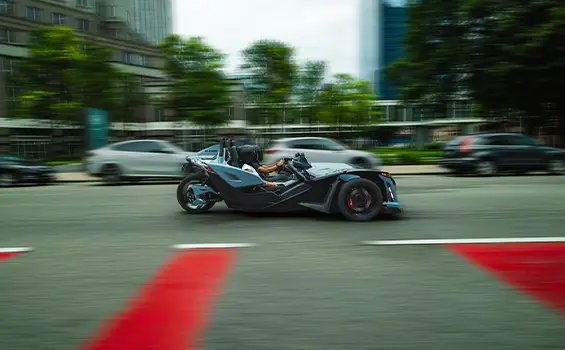 Side profile of a 2026 Polaris Slingshot Signature Edition 3-wheeled roadster cruising down a city street.