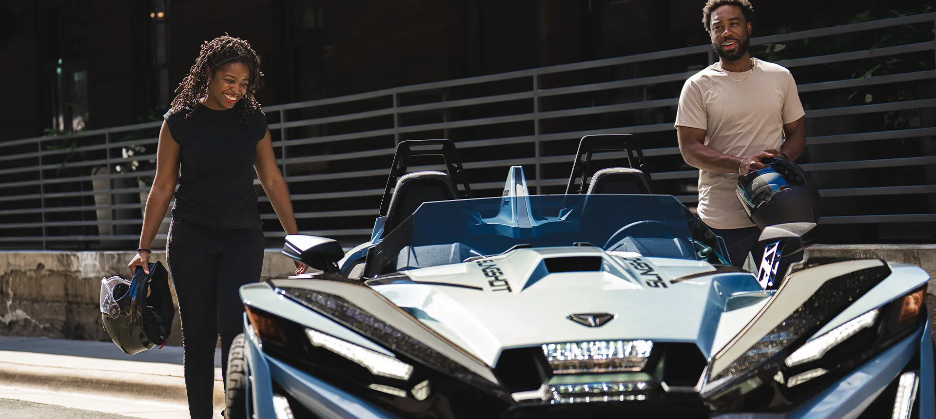 Dos personas con cascos caminando hacia un Roadster de tres ruedas Polaris Slingshot Signature Edition de 2026.