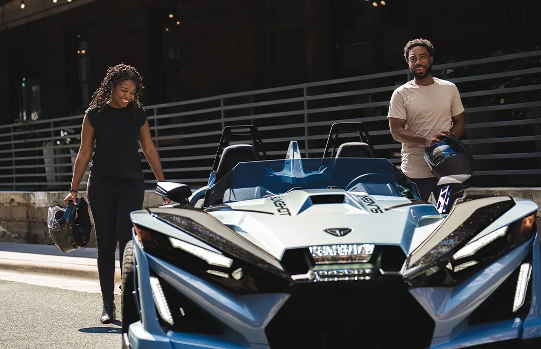 Dos personas con cascos caminando hacia un Roadster de tres ruedas Polaris Slingshot Signature Edition de 2026.