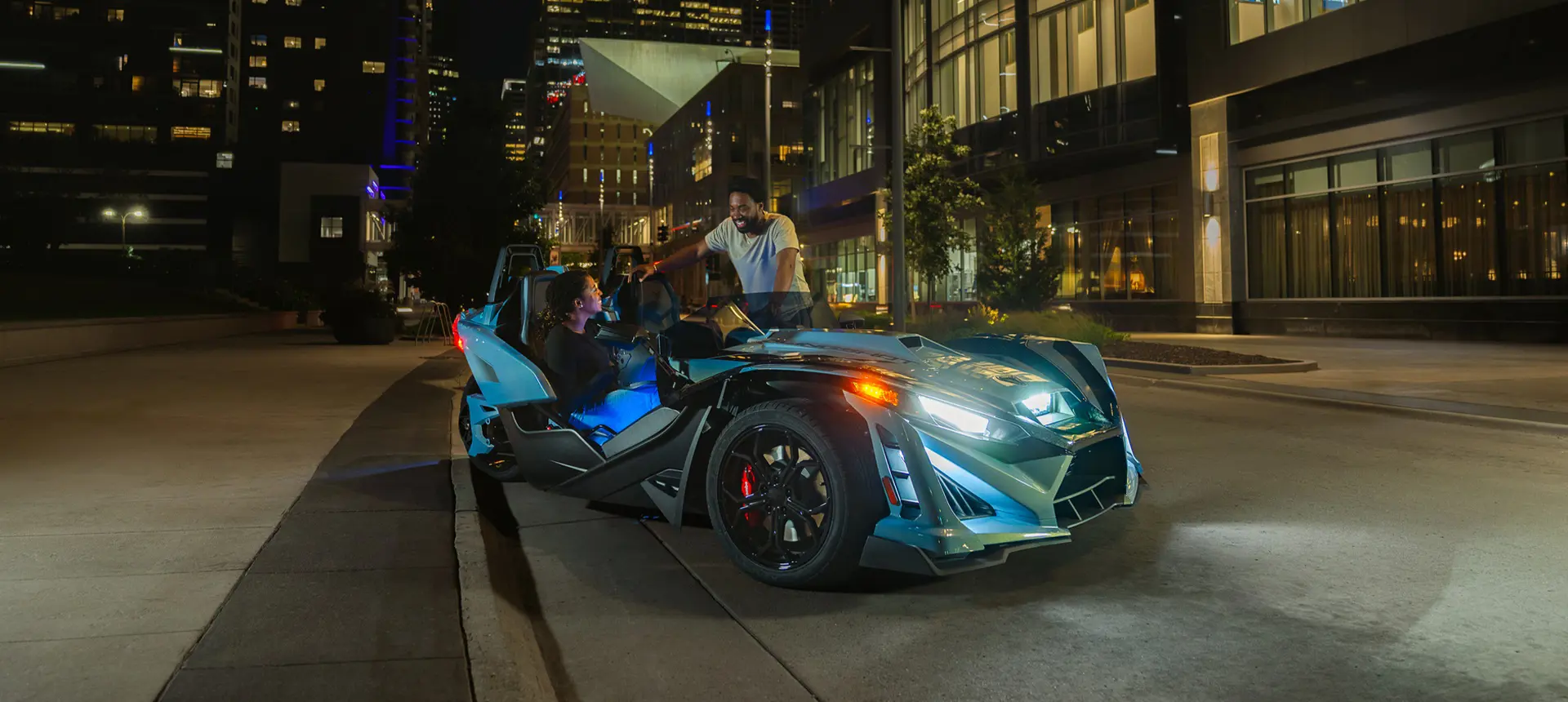 Un Roadster de tres ruedas Polaris Slingshot Signature Edition 2026 estacionado en una calle de la ciudad por la noche.