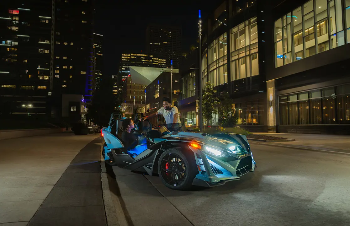 Un Roadster de tres ruedas Polaris Slingshot Signature Edition 2026 estacionado en una calle de la ciudad por la noche.