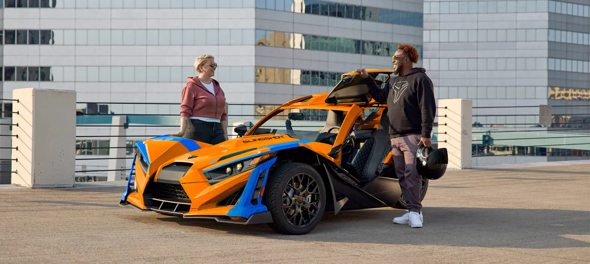 2 people standing near a 2026 Polaris Slingshot SL three-wheel motorcycle parked in a city.