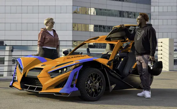 2 people standing near a 2026 Polaris Slingshot SL three-wheel motorcycle parked in a city.