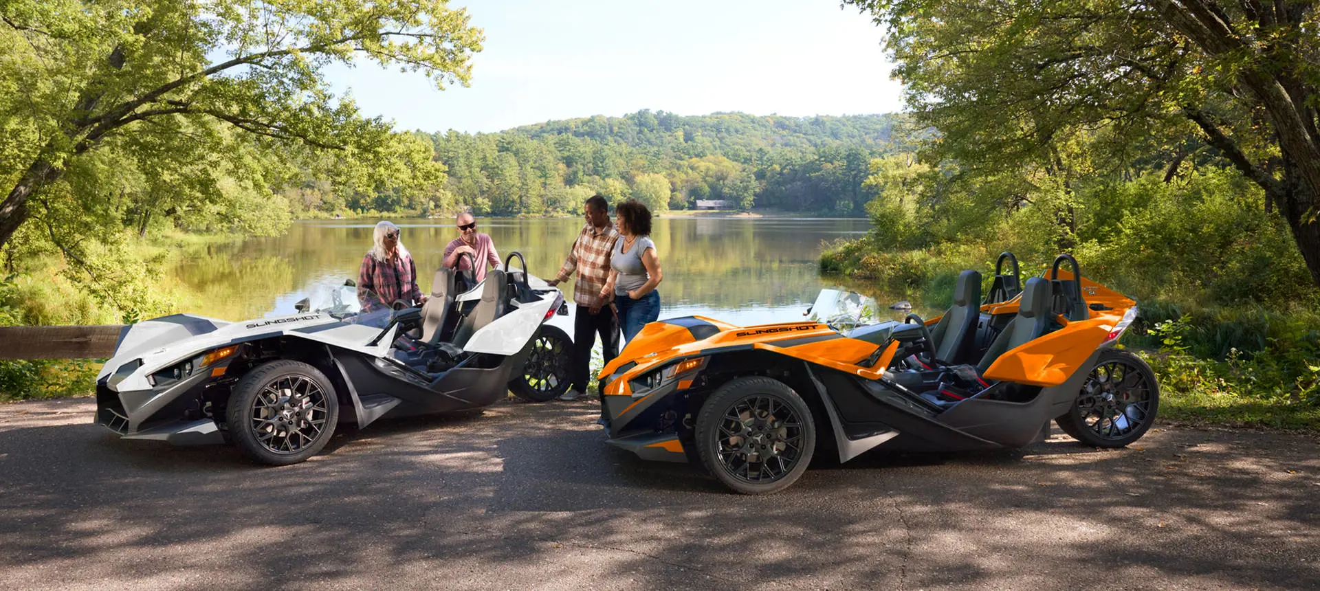 People standing near their parked 2026 Polaris Slingshot SL three-wheel motorcycles near a lake.