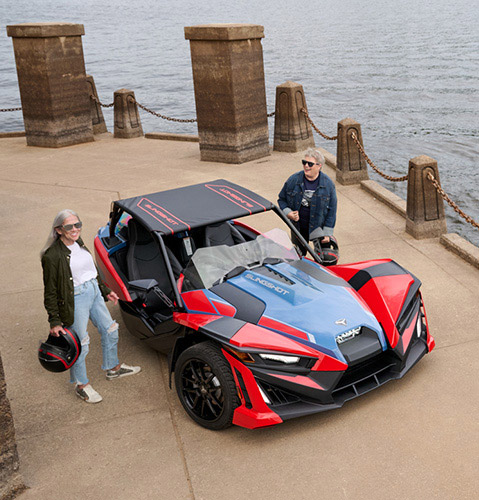 Three parked Polaris Slingshot vehicles in front of brick building.