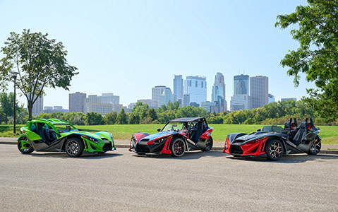 Trois véhicules Polaris Slingshot stationnés devant un bâtiment en brique.