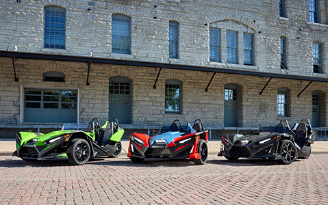 Three parked Polaris Slingshot vehicles in front of brick building.