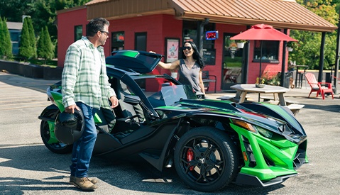 Dos vehículos modernos Polaris Slingshot de tres ruedas acelerando en un camino soleado, rodeados de una vegetación exuberante.