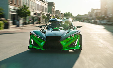 Green Polaris Slingshot three wheel motorcycle driving on an open highway, highlighting bold design and exhilarating performance.
