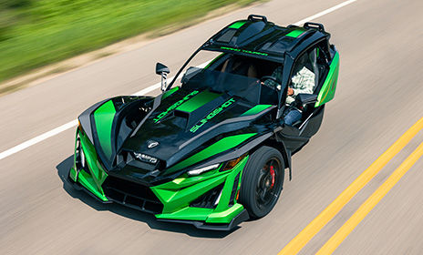 Green Polaris Slingshot three wheel motorcycle driving on an open highway, highlighting bold design and exhilarating performance.
