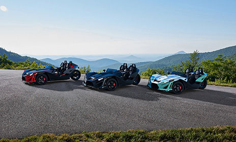 Three Polaris Slingshot three wheel motorcycles parked at a scenic overlook, showcasing bold colors and open-air freedom.
