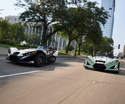 Two Polaris Slingshot three wheel motorcycles on a group drive in the city.

