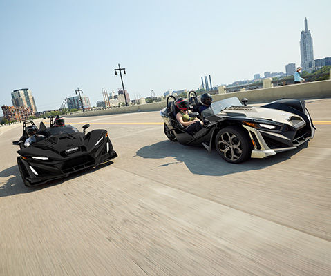Two Polaris Slingshot three wheel motorcycles on a group drive in the city.
