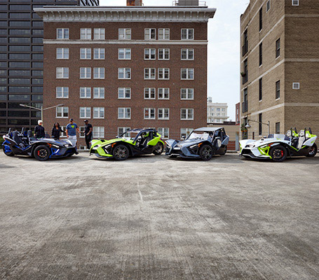 Four colorful Polaris Slingshot roadsters displayed with four people on an urban rooftop.