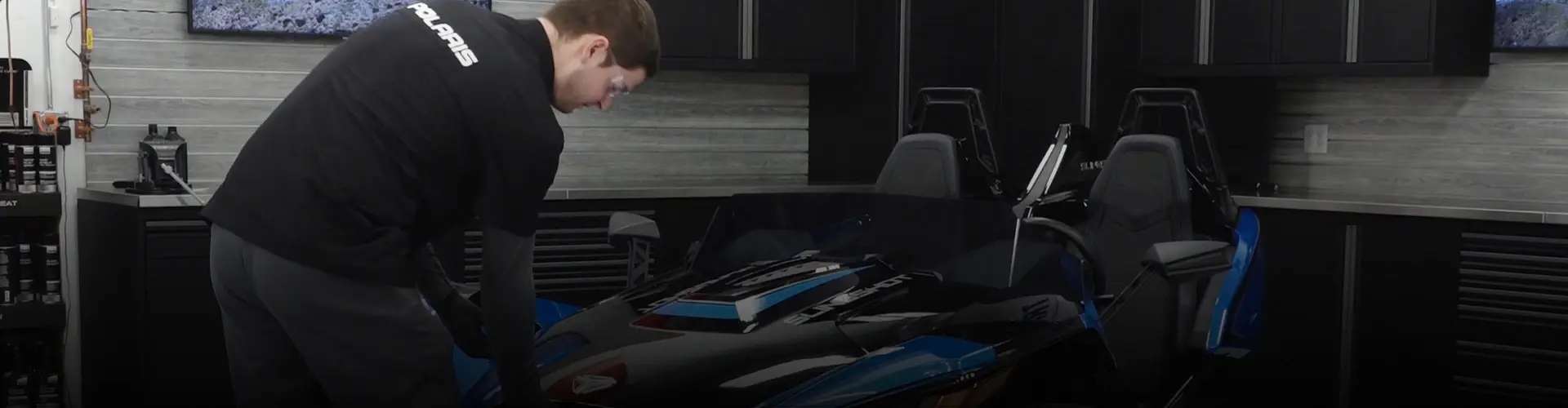 Technician performing maintenance on a blue and black Polaris Slingshot in a workshop.