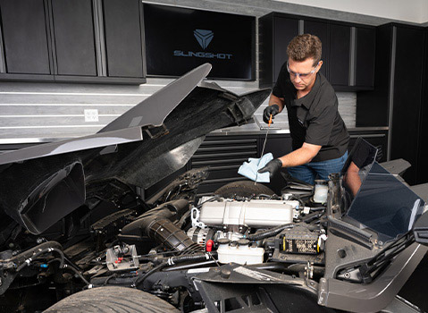 Technician checking the oil level in a Polaris Slingshot engine during routine maintenance in a garage.