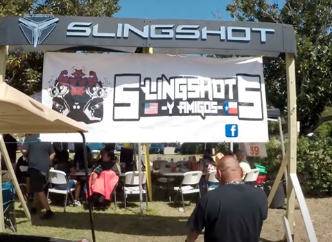 Slingshot y Amigos banner displayed above an outdoor gathering beneath a Polaris Slingshot event sign.