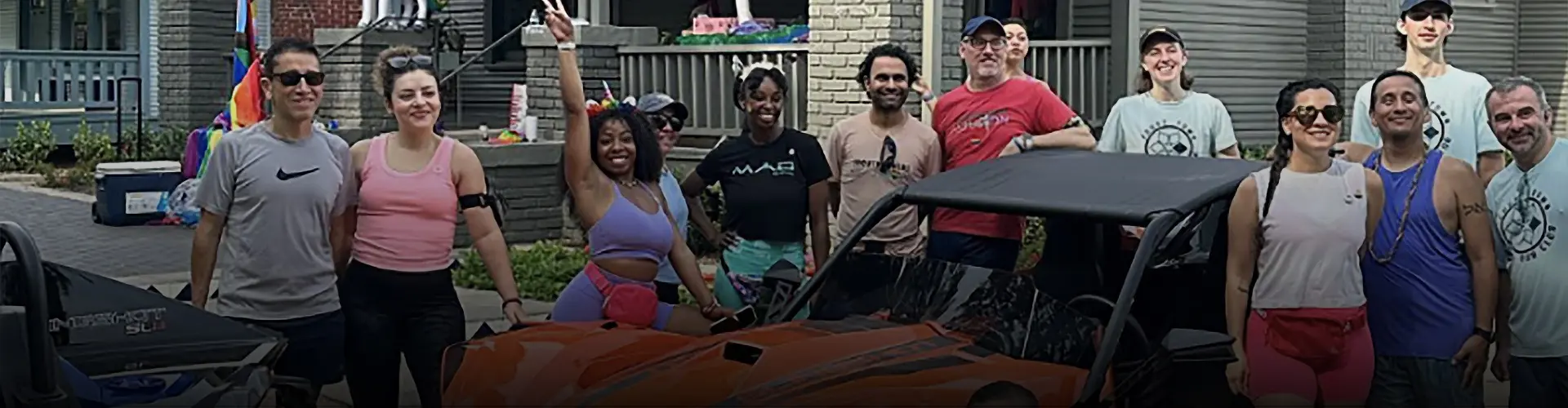Group gathered around an orange Polaris Slingshot autocycle at an outdoor neighborhood event.