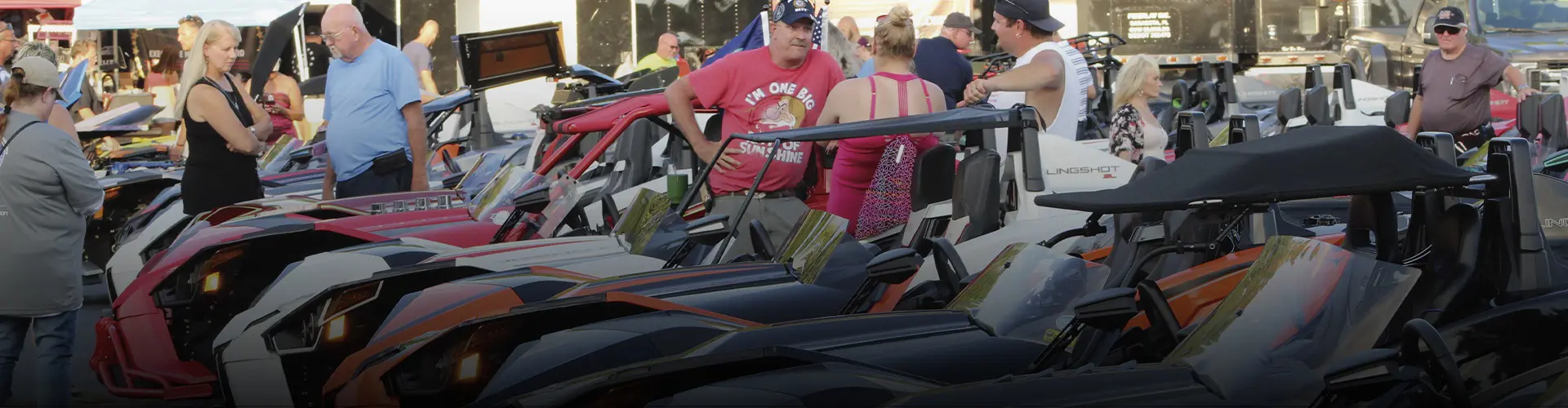 Polaris Slingshot three-wheel vehicles displayed as attendees explore an outdoor automotive event.