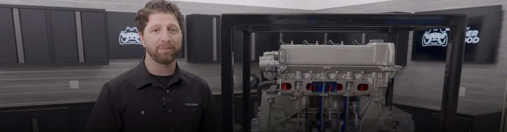 Jake Stock presenting a cutaway Polaris Slingshot engine inside a garage workshop with Polaris branding and storage cabinets in the background.
